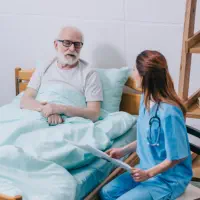 A female caregiver looking to a senior man laying on the bed