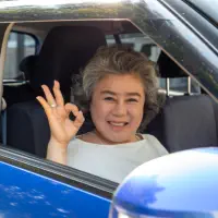 A senior woman inside a car doing the okay pose