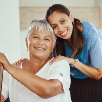 A senior woman sitting and a female caregiver smiling together