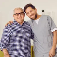 A male caregiver and a senior man smiling together