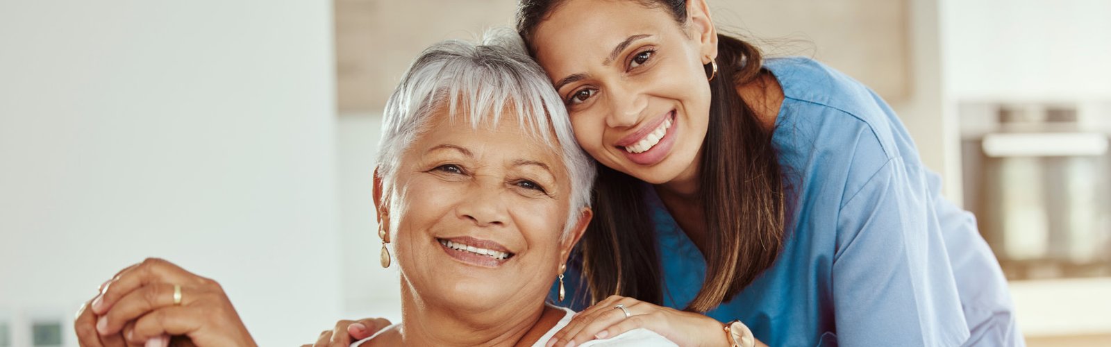 A senior woman sitting and a female caregiver smiling together