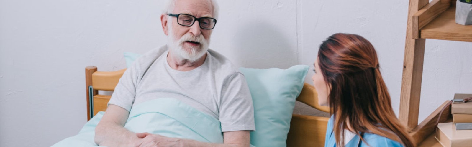 A female caregiver looking to a senior man laying on the bed