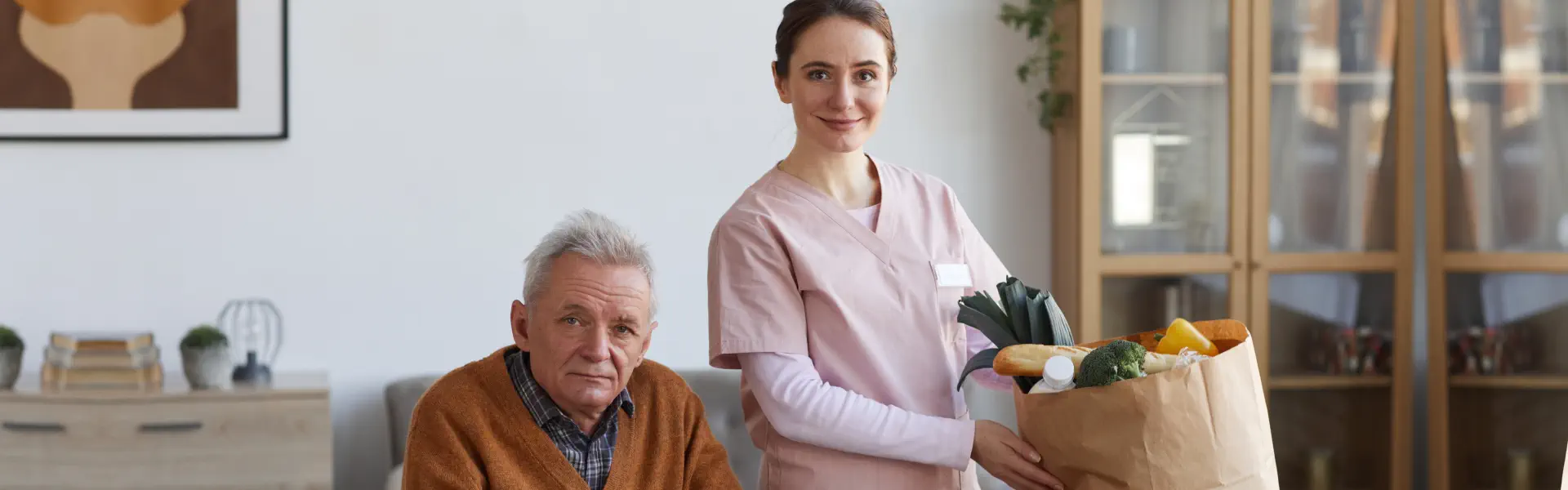 A senior man sitting on and a female caregiver preparing the foods in the bag