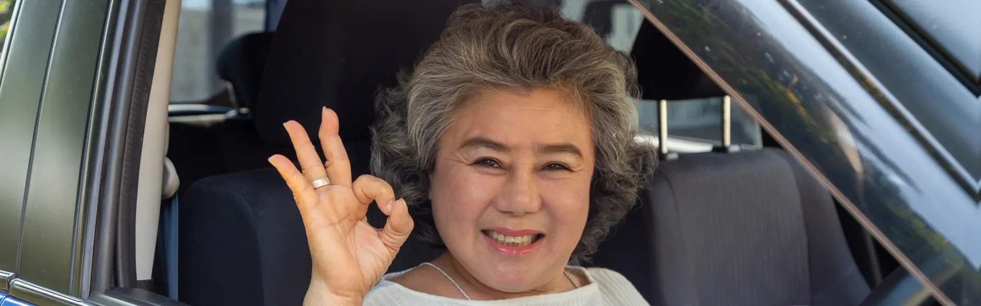 A senior woman inside a car doing the okay pose