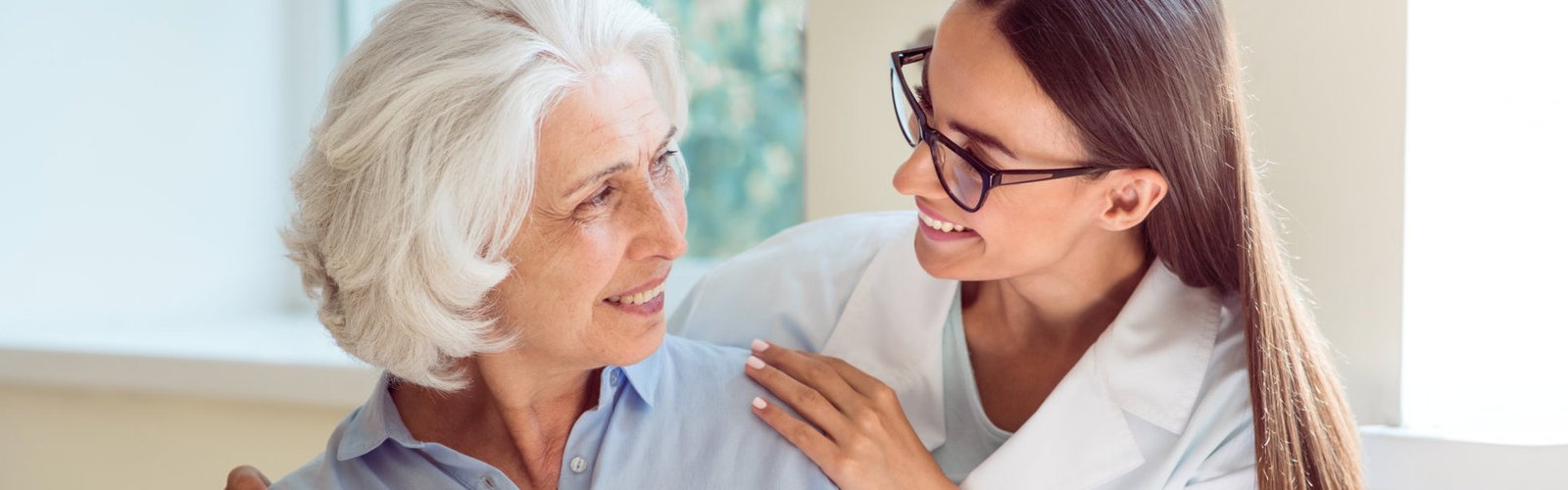 A female wearing eyeglasses holding the shoulders of a senior woman
